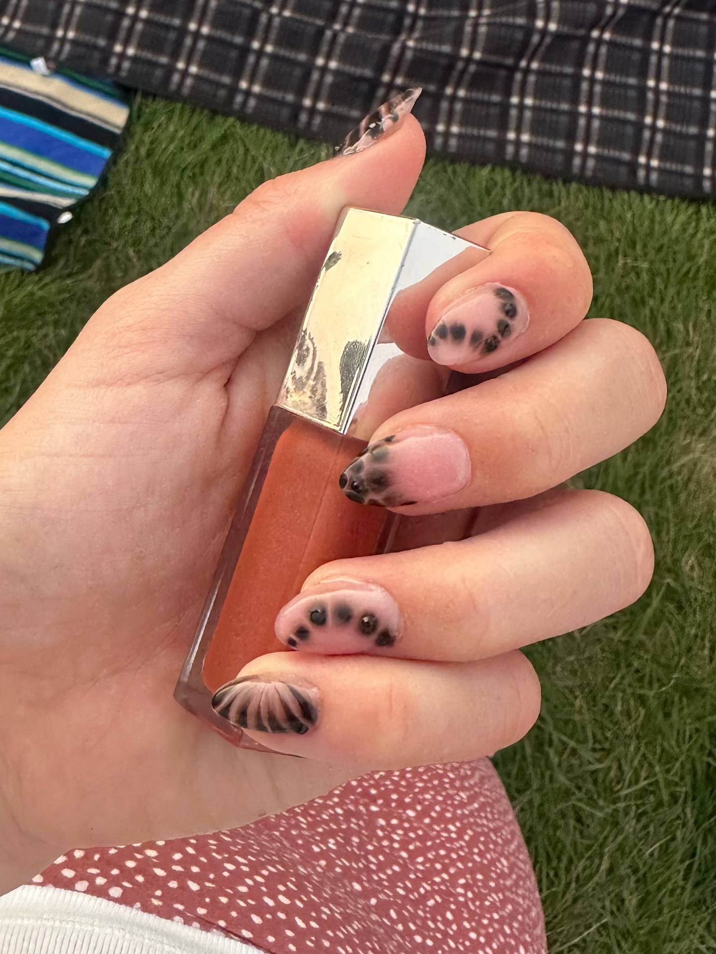Painted nails holding lip gloss on a green grass background