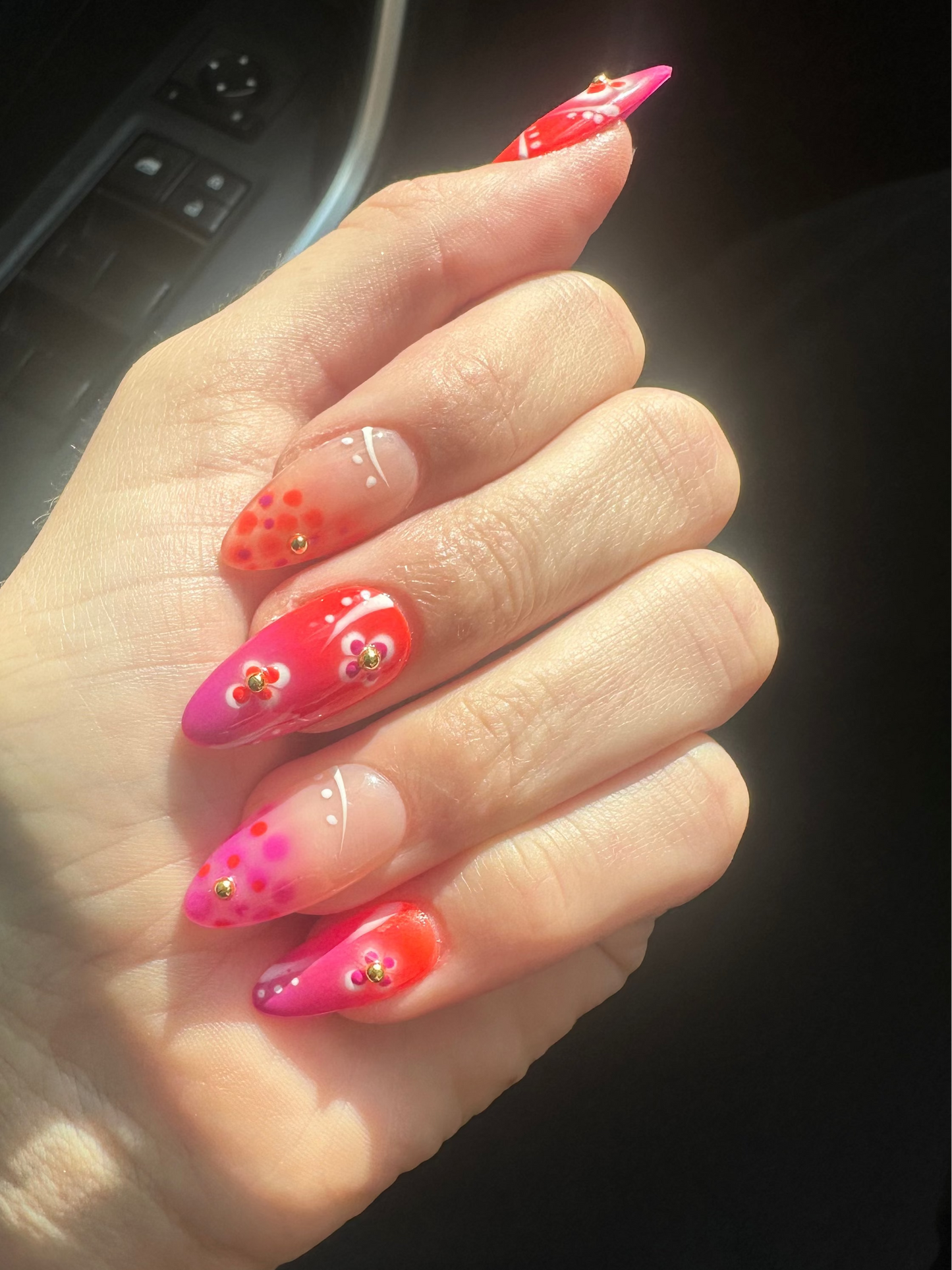 Hand with pink and orange nail polish inside a vehicle.