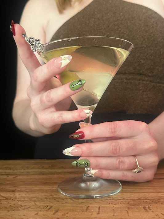 Hand holding a martini glass with a olive garnish on a wooden surface